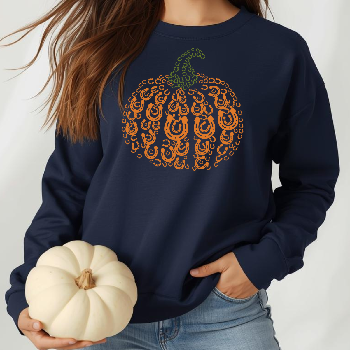 Person wearing a navy sweatshirt with a decorative pumpkin design, holding a small white pumpkin.