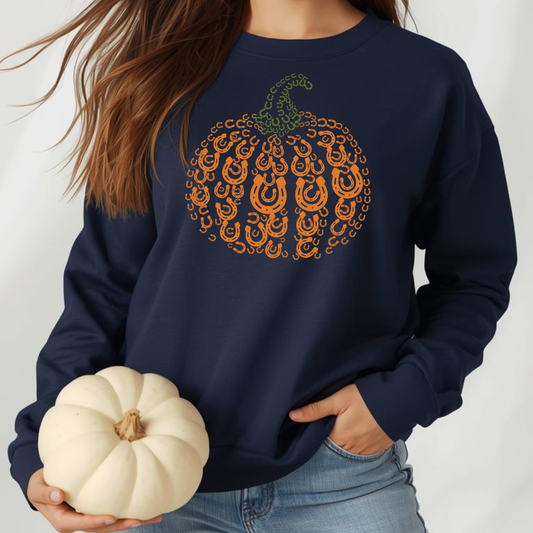 Person wearing a navy sweatshirt with a decorative pumpkin design, holding a small white pumpkin.
